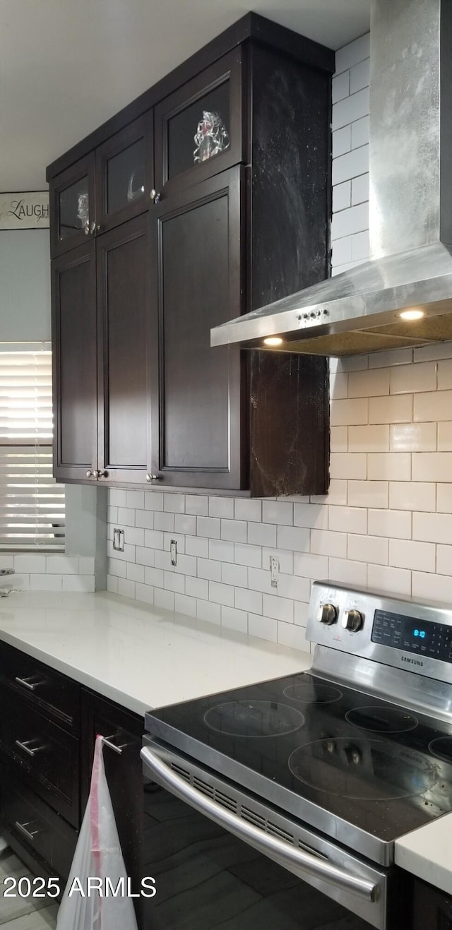 kitchen featuring stainless steel range with electric stovetop, backsplash, dark brown cabinetry, and wall chimney exhaust hood