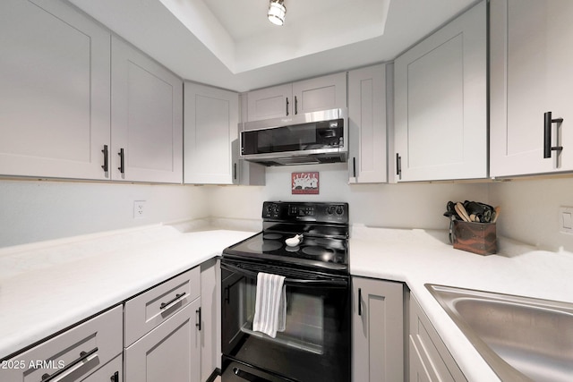 kitchen with electric range, stainless steel microwave, light countertops, and a tray ceiling