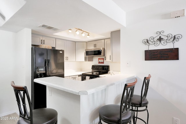 kitchen featuring black appliances, a kitchen breakfast bar, a peninsula, and light countertops