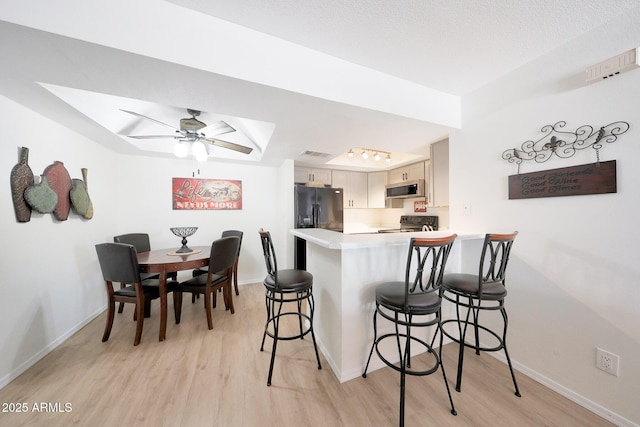 kitchen with a tray ceiling, light wood-type flooring, black appliances, and baseboards