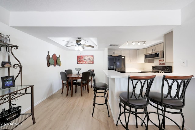 kitchen with black appliances, light countertops, ceiling fan, light wood-style flooring, and a kitchen bar