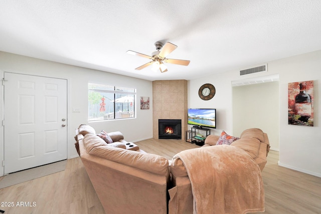 living area featuring light wood-type flooring, a fireplace, and a ceiling fan