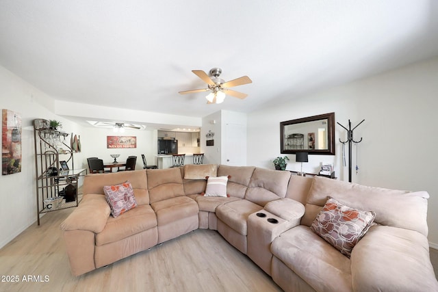 living area featuring light wood-type flooring, a ceiling fan, and baseboards