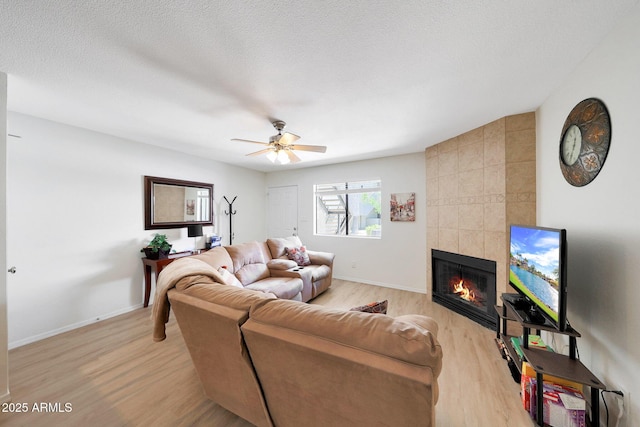 living room featuring light wood-type flooring, a fireplace, ceiling fan, and baseboards