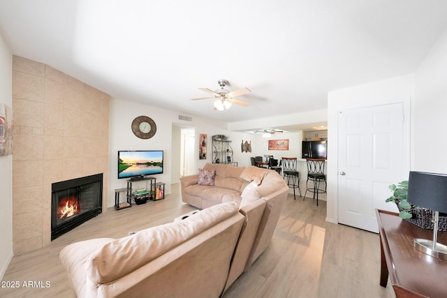 living area featuring ceiling fan, light wood-type flooring, and a tiled fireplace