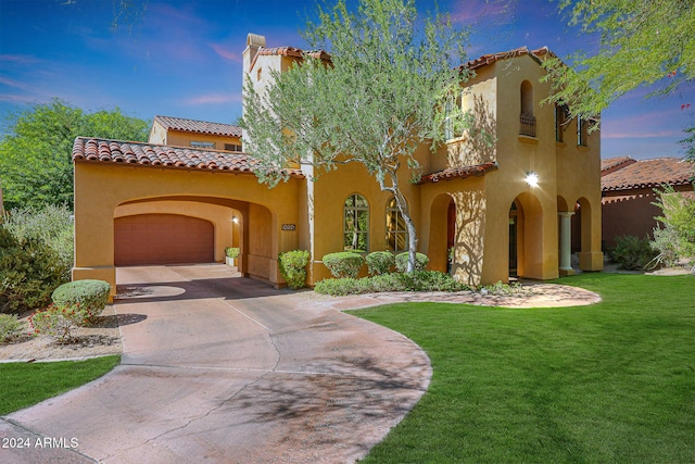 mediterranean / spanish house featuring an attached garage, concrete driveway, a tiled roof, stucco siding, and a front yard