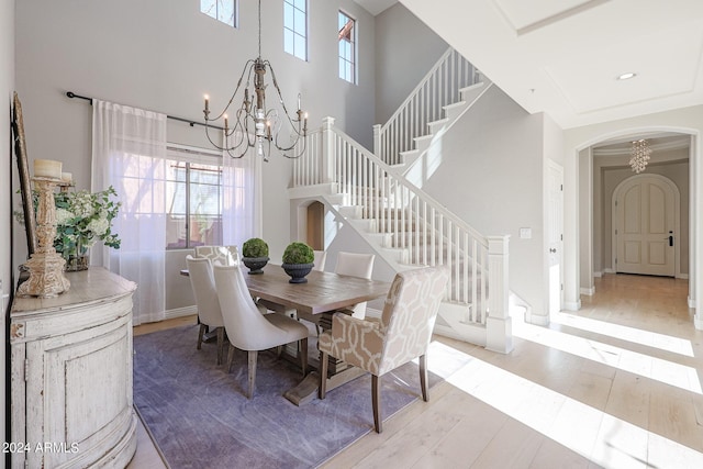 dining room featuring arched walkways, a towering ceiling, wood finished floors, an inviting chandelier, and stairs