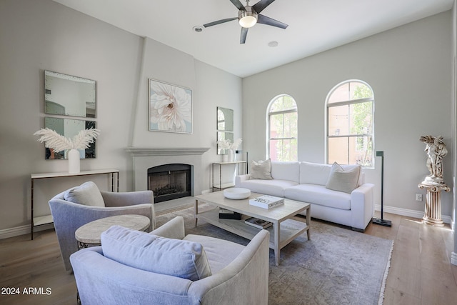 living area featuring a ceiling fan, a high end fireplace, baseboards, and wood finished floors