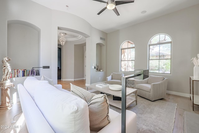 living room featuring arched walkways, a ceiling fan, light wood-style flooring, and baseboards