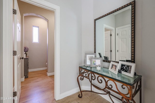 corridor featuring light wood-type flooring, baseboards, and arched walkways