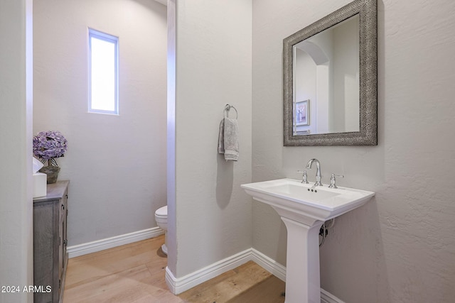 half bath featuring toilet, a sink, baseboards, and wood finished floors