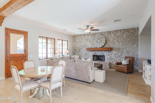 dining room featuring baseboards, visible vents, a ceiling fan, a stone fireplace, and light wood-style floors