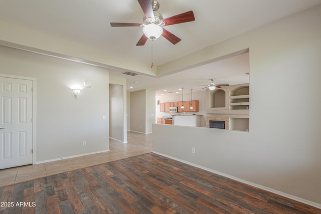 unfurnished living room featuring ceiling fan, built in features, and wood-type flooring