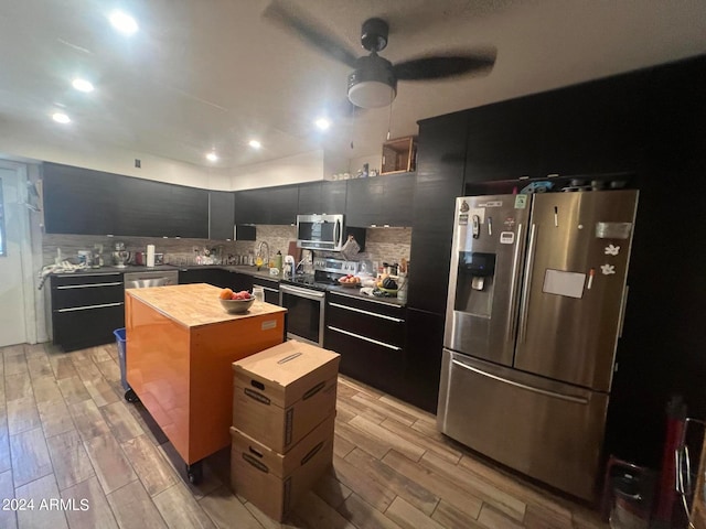 kitchen featuring appliances with stainless steel finishes, backsplash, a kitchen island, ceiling fan, and light hardwood / wood-style flooring