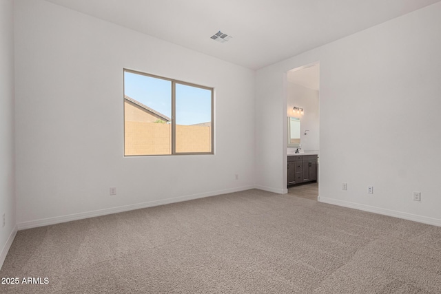 unfurnished bedroom with light colored carpet, visible vents, a sink, ensuite bath, and baseboards