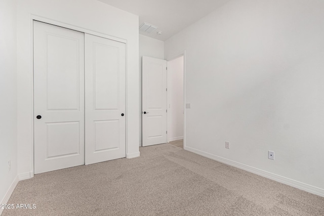 unfurnished bedroom with a closet, light carpet, and baseboards