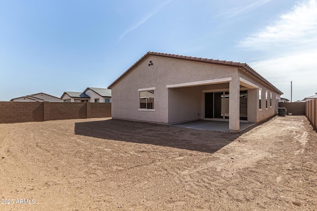 rear view of house featuring stucco siding, a fenced backyard, a tiled roof, and a patio