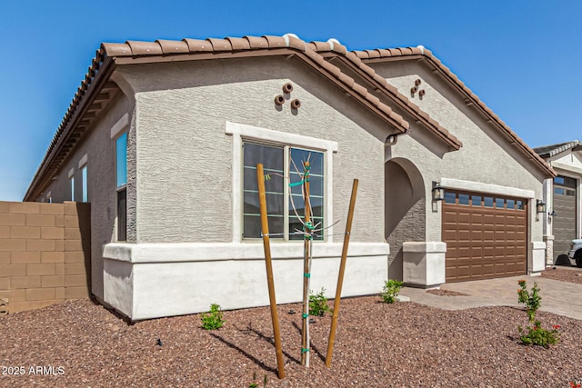 view of front of house featuring a tile roof, stucco siding, fence, a garage, and driveway