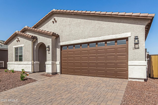 view of front of property with decorative driveway, a tile roof, stucco siding, an attached garage, and fence