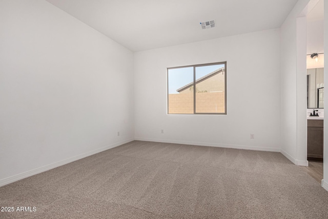 empty room featuring light carpet, a sink, visible vents, and baseboards