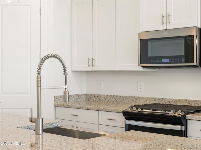 kitchen featuring white cabinets, light stone counters, stainless steel microwave, gas range oven, and a sink