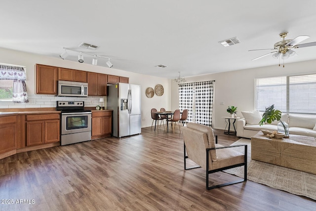 2286 E Mohave Ln, Apache Junction, AZ 85119 - kitchen featuring appliances with stainless steel finishes, open floor plan, brown cabinetry, wood finished floors, and tasteful backsplash