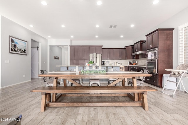 kitchen featuring a barn door, dark brown cabinets, light hardwood / wood-style floors, and decorative backsplash