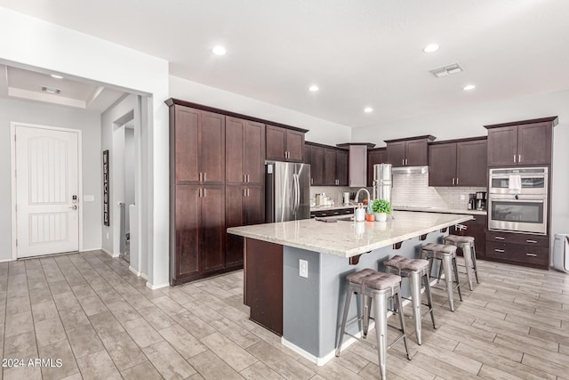 kitchen featuring a kitchen breakfast bar, decorative backsplash, light hardwood / wood-style floors, stainless steel appliances, and a center island with sink