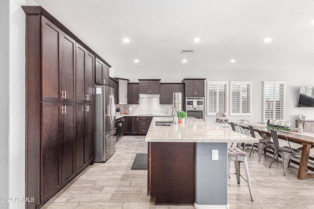 kitchen featuring sink, a breakfast bar area, appliances with stainless steel finishes, backsplash, and an island with sink