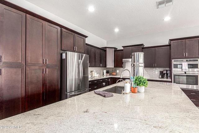 kitchen featuring tasteful backsplash, appliances with stainless steel finishes, light stone countertops, and sink