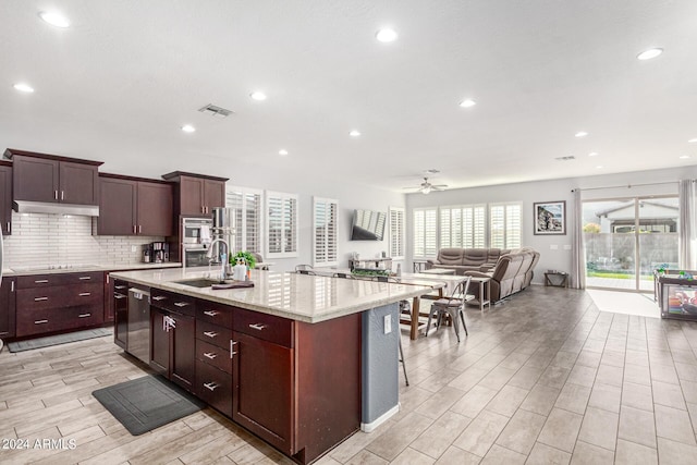 kitchen with sink, a breakfast bar area, stainless steel appliances, a center island with sink, and decorative backsplash