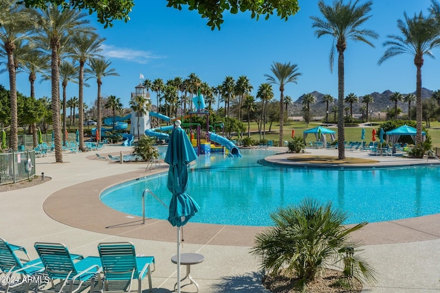 view of swimming pool with a water slide, a playground, and a patio