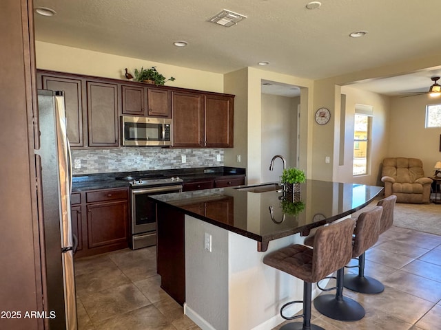 kitchen with sink, a center island with sink, decorative backsplash, a breakfast bar area, and stainless steel appliances