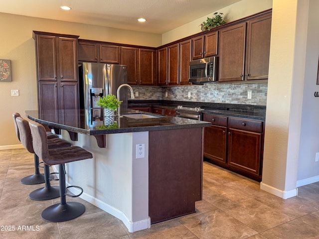 kitchen with appliances with stainless steel finishes, sink, backsplash, a kitchen bar, and a center island with sink