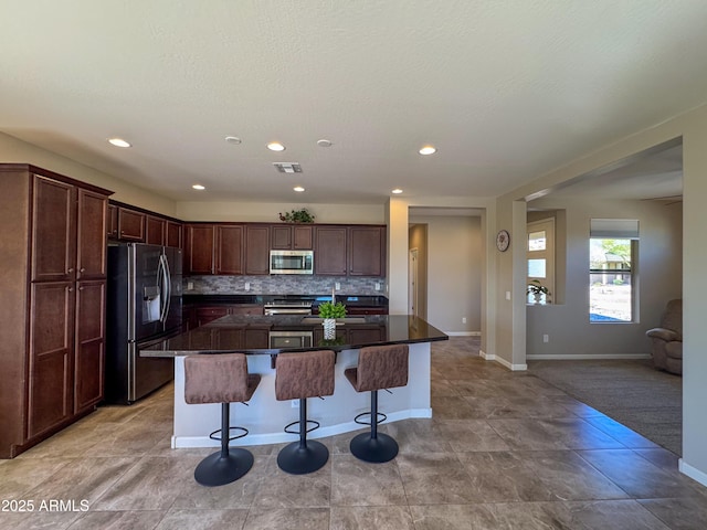 kitchen with appliances with stainless steel finishes, a breakfast bar, a kitchen island, decorative backsplash, and dark brown cabinetry