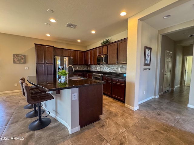 kitchen with appliances with stainless steel finishes, sink, backsplash, a kitchen bar, and a center island with sink