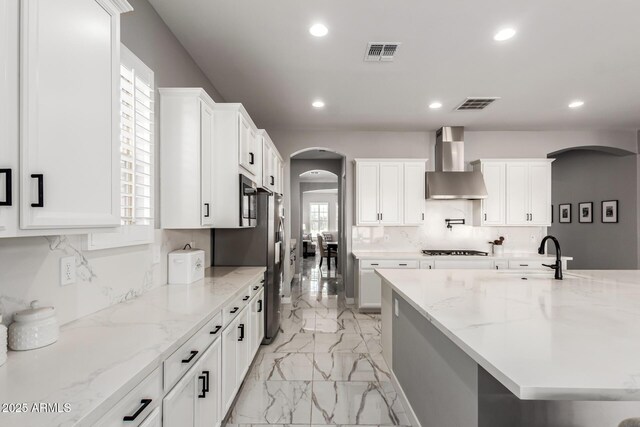 kitchen featuring light stone countertops, white cabinetry, decorative backsplash, and wall chimney range hood