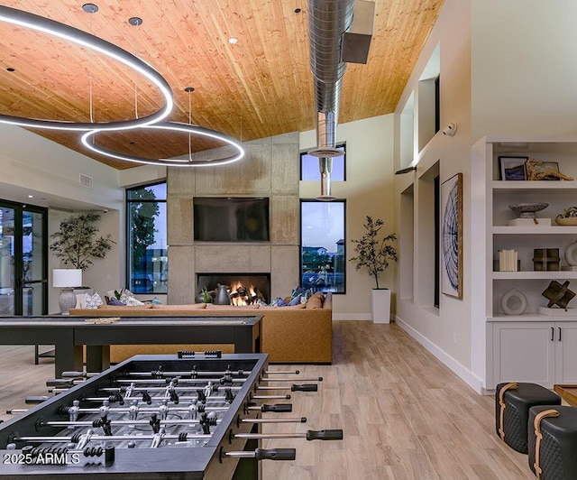 playroom featuring wood-type flooring, a high ceiling, a large fireplace, and built in shelves