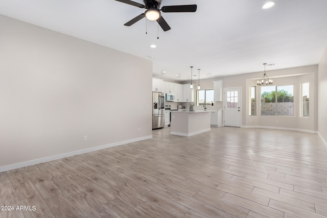 unfurnished living room with ceiling fan with notable chandelier and light hardwood / wood-style floors