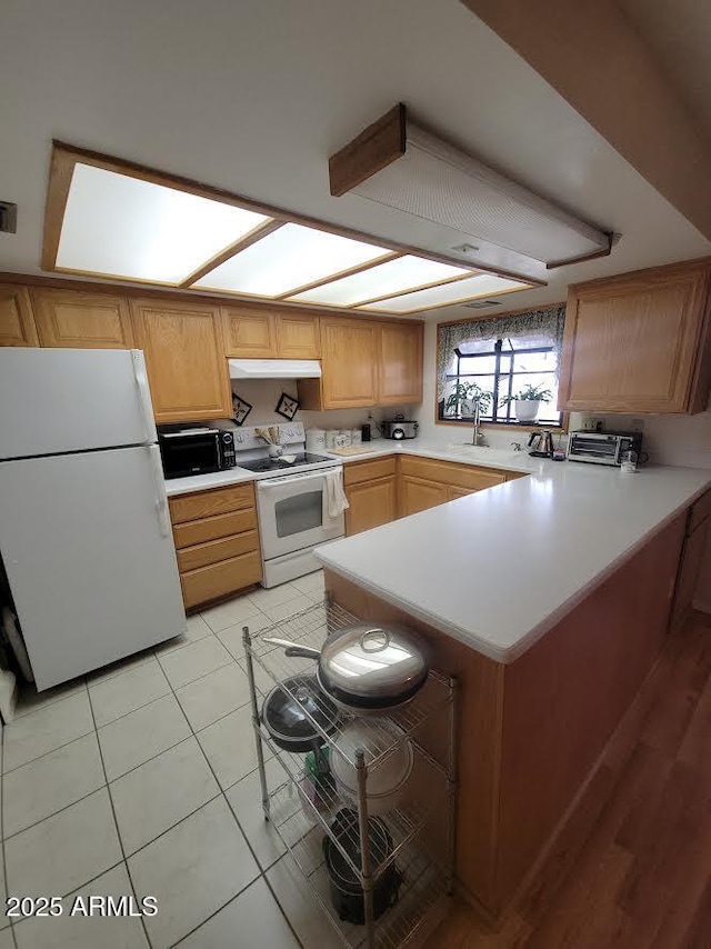 kitchen featuring light countertops, light tile patterned flooring, white appliances, a peninsula, and under cabinet range hood