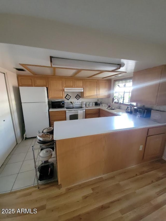 kitchen featuring under cabinet range hood, a peninsula, white appliances, light wood-style floors, and light countertops