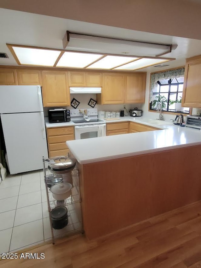 kitchen featuring light countertops, white appliances, light brown cabinets, and under cabinet range hood