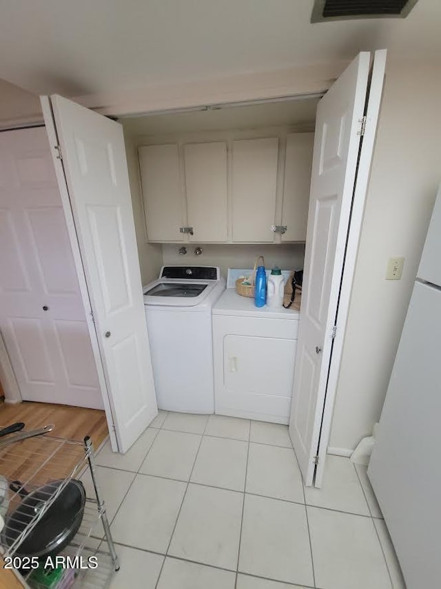 laundry area featuring visible vents, light tile patterned flooring, washing machine and clothes dryer, and cabinet space