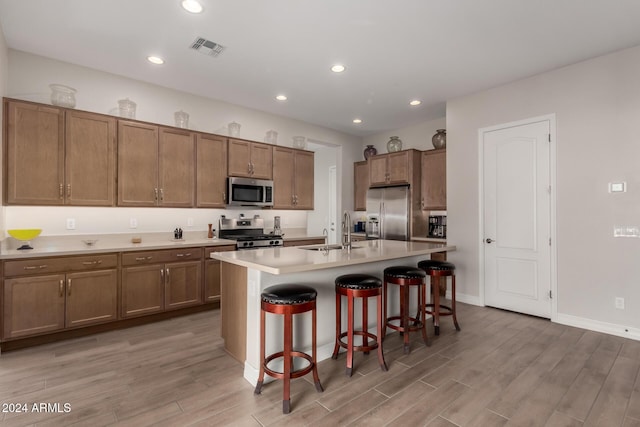 kitchen with sink, a kitchen breakfast bar, light hardwood / wood-style flooring, an island with sink, and appliances with stainless steel finishes