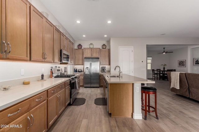 kitchen featuring sink, a kitchen bar, a kitchen island with sink, appliances with stainless steel finishes, and light wood-type flooring