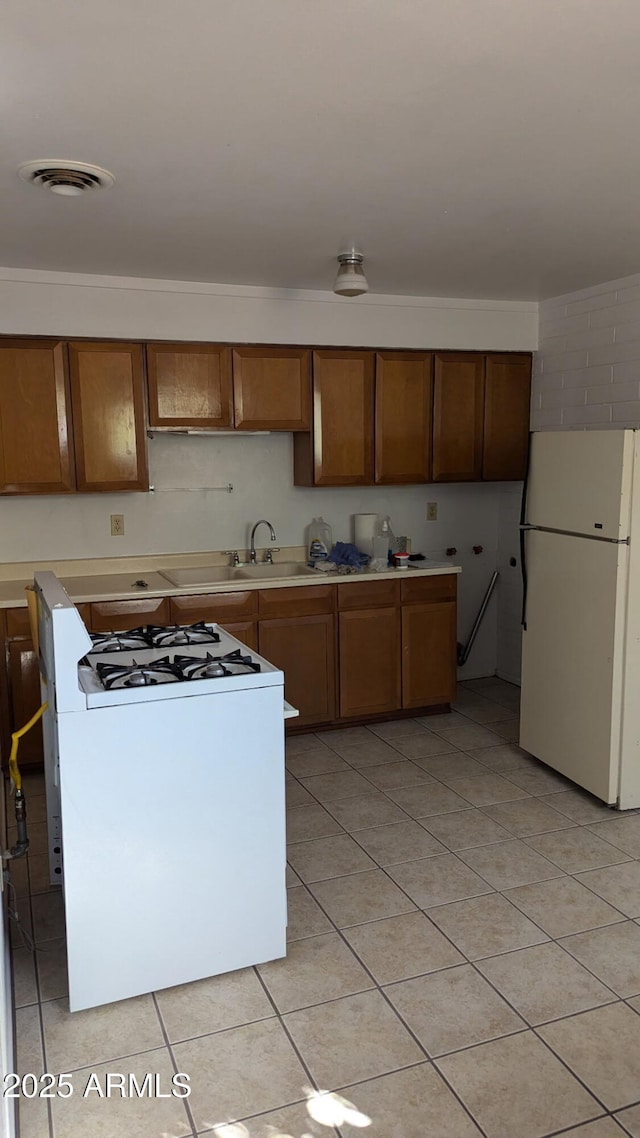 kitchen featuring light tile patterned flooring, white appliances, a sink, light countertops, and brown cabinets