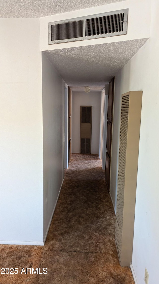 hall with carpet floors, a heating unit, visible vents, and a textured ceiling