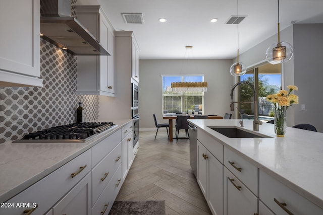 kitchen with backsplash, sink, wall chimney exhaust hood, light parquet floors, and hanging light fixtures