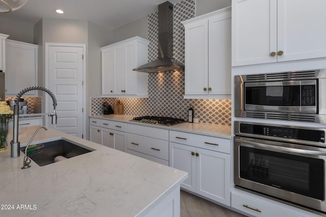 kitchen featuring backsplash, light stone counters, stainless steel appliances, wall chimney range hood, and white cabinets