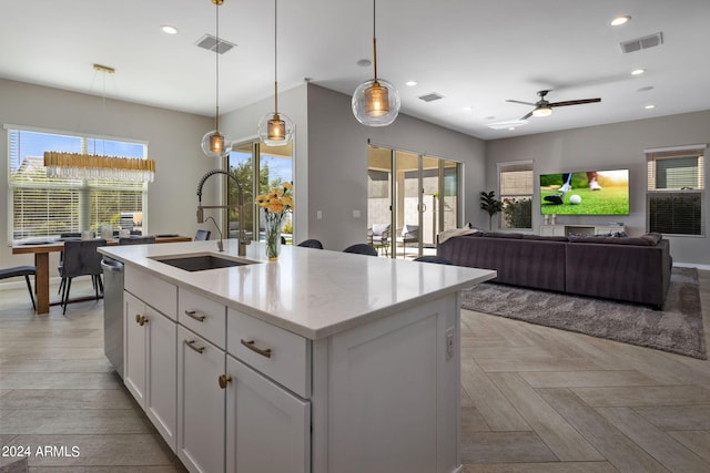 kitchen featuring light parquet flooring, a kitchen island with sink, white cabinetry, sink, and decorative light fixtures